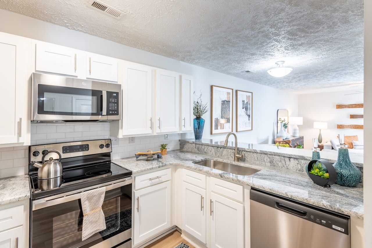 Modern kitchen with white cabinets, stainless steel appliances, and a view into a bright living area.