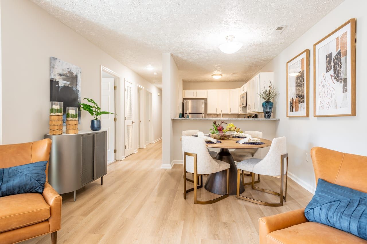 A modern dining and living area with tan chairs, round table, and open kitchen in neutral tones.
