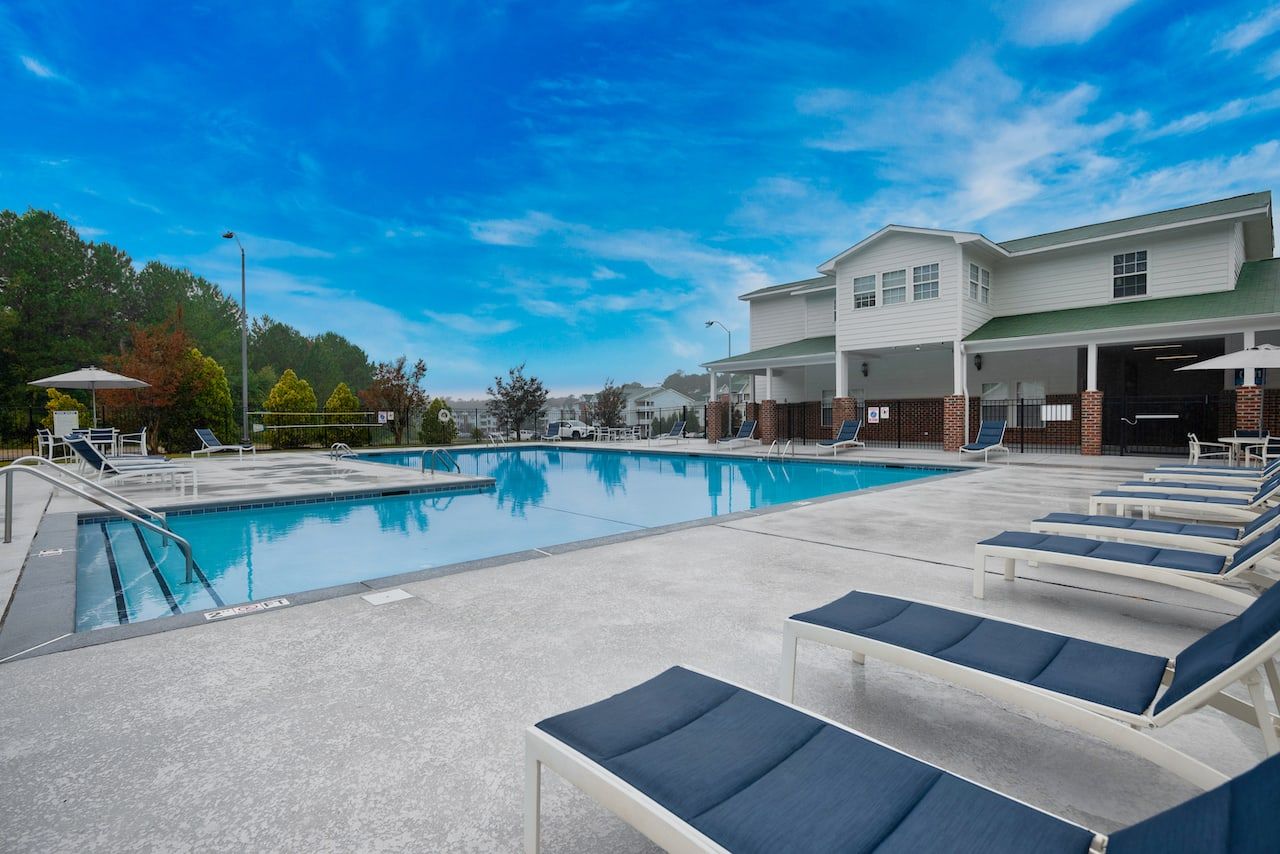 Outdoor swimming pool with lounge chairs and umbrellas beside a residential building under a blue sky.